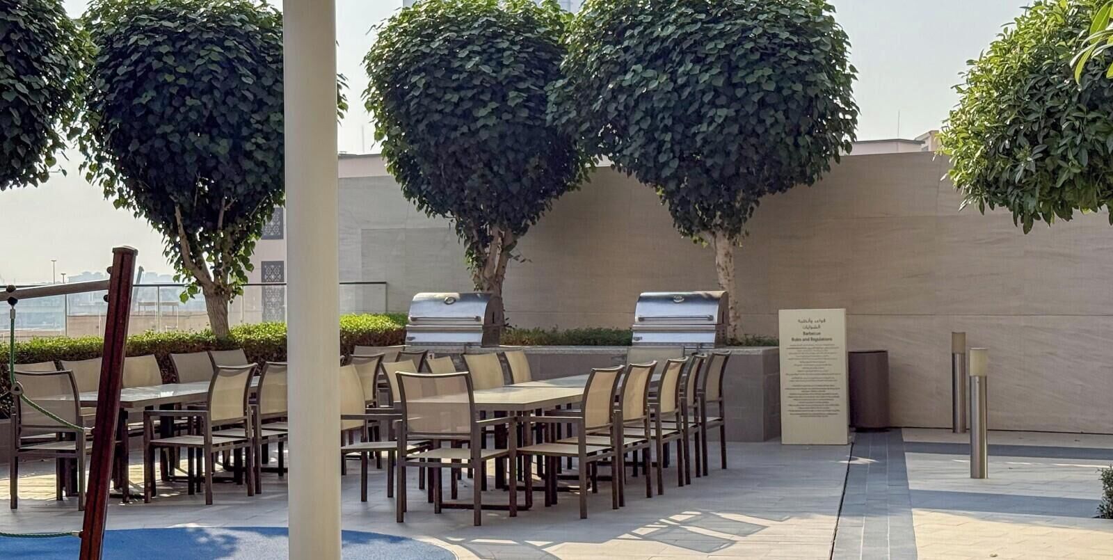 Un espace de restauration en plein air, avec des tables et des chaises, entouré d’arbres et d’un mur.