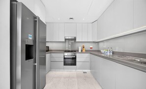 Una cocina moderna con electrodomésticos de acero inoxidable, armarios blancos y piso de mármol.