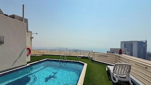 Piscina no terraço com vista para o horizonte da cidade, placa de proibição de mergulho e boia salva-vidas.