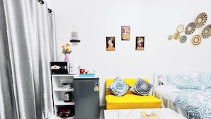 A compact living space with a kitchenette, a sofa with patterned cushions, a coffee table, and wall art. - Room-105 Budget Room, Wifi&utilities Ban (Bangkok)