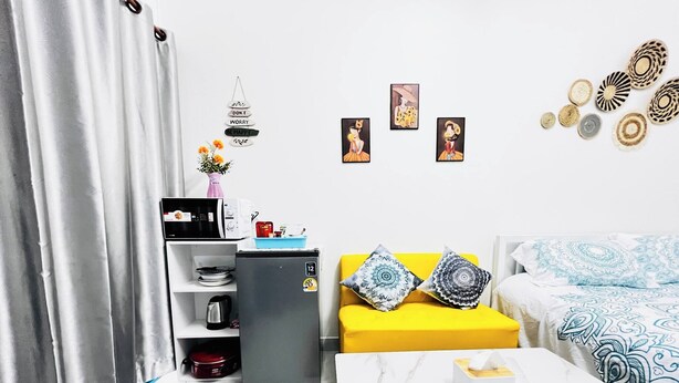 A compact living space with a kitchenette, a sofa with patterned cushions, a coffee table, and wall art. - Room-105 Budget Room, Wifi&utilities Ban (Bangkok)