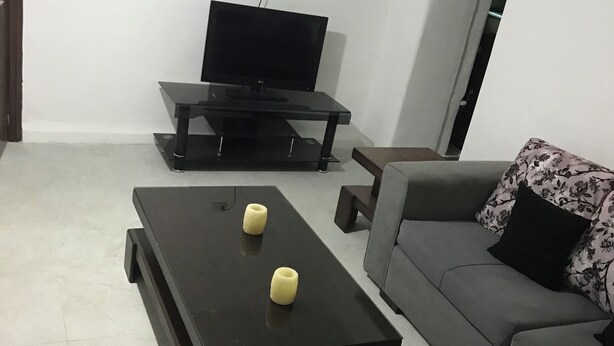 Een woonkamer met een flatscreen televisie op een standaard, een bank met bloemkussens en een salontafel met twee kaarsen.