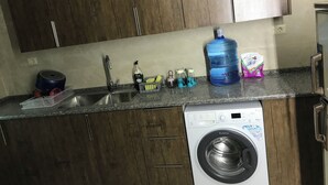 Een keuken met houten kastjes, een roestvrijstalen spoelbak, een wasmachine en diverse keukenbenodigdheden op het aanrecht.