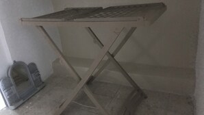 Een metalen tafel met metalen blad en een eenvoudig kruisframe, geplaatst tegen een effen muur.
