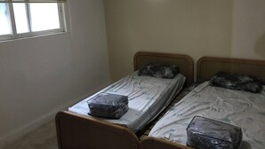 Een slaapkamer met twee bedden, een raam met zonwering en een hanglamp.
