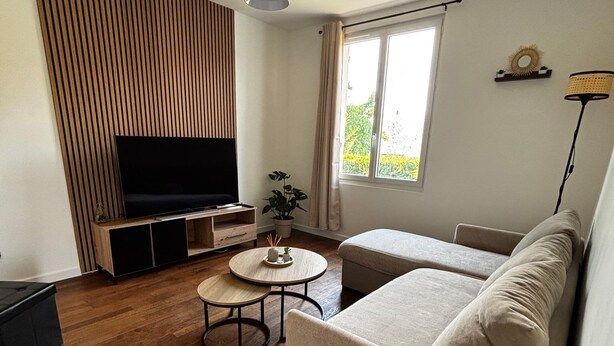 Een woonkamer met een bank, televisie, houten vloer en een raam.