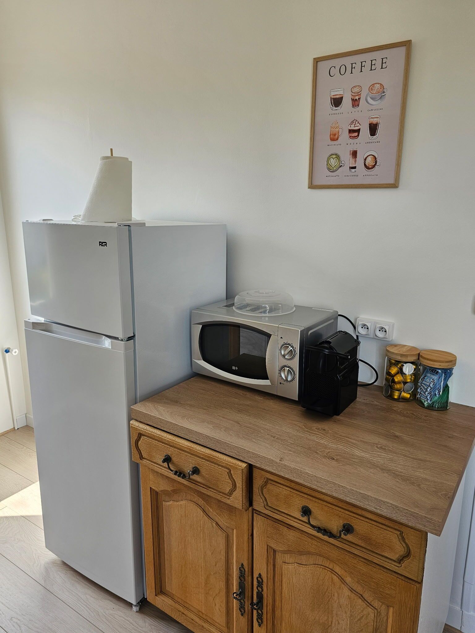 Eine Küche mit Kühlschrank, Mikrowelle, Kaffeemaschine und einer Wanddekoration zum Thema Kaffee.