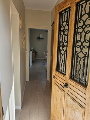 A hallway with a wooden door with black metal detailing, a radiator, and a chair in the background. - Entire Rental: La Caze (Saint-Gervais-la-Forêt)