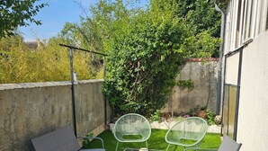 Een terras met tuinmeubilair, een tafel, en een kleine tuin met kunstgras en beplanting.