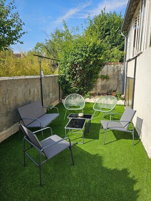 A patio with outdoor furniture, a table, and a small garden area with artificial grass and plants. - Entire Rental: La Caze (Saint-Gervais-la-Forêt)