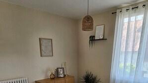 Een eetruimte met een houten tafel, witte stoelen, een hanglamp, een radiator en een raam met gordijnen.