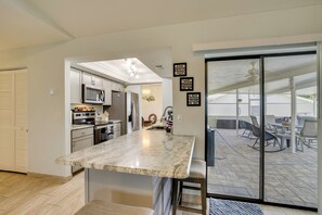 A modern kitchen with a marble countertop, stainless steel appliances, and a sliding glass door leading to an outdoor patio area. - On Preserved Land w/ Pool & Trails! Cape Coral Gem (Cape Coral)