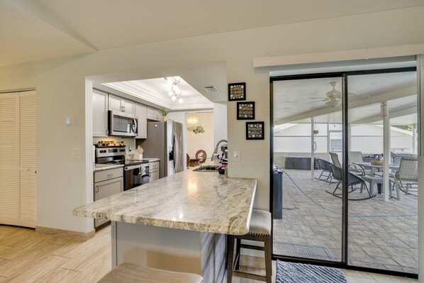 A modern kitchen with a marble countertop, stainless steel appliances, and a sliding glass door leading to an outdoor patio area. - On Preserved Land w/ Pool & Trails! Cape Coral Gem (Cape Coral)