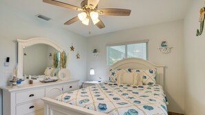 Quarto com cama, penteadeira, mesa de cabeceira, ventilador de teto e uma janela.