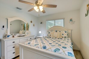 Ein Schlafzimmer mit Bett, Kommode, Nachttisch, Deckenventilator und Fenster.