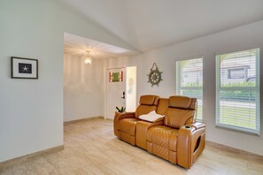 A spacious room with a leather sofa, a framed picture, a wall-mounted light fixture, and a window with blinds. - On Preserved Land w/ Pool & Trails! Cape Coral Gem (Cape Coral)