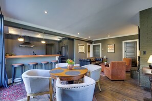 A modern kitchen with bar stools, a dining table with chairs, and a living area with a sofa and armchairs.