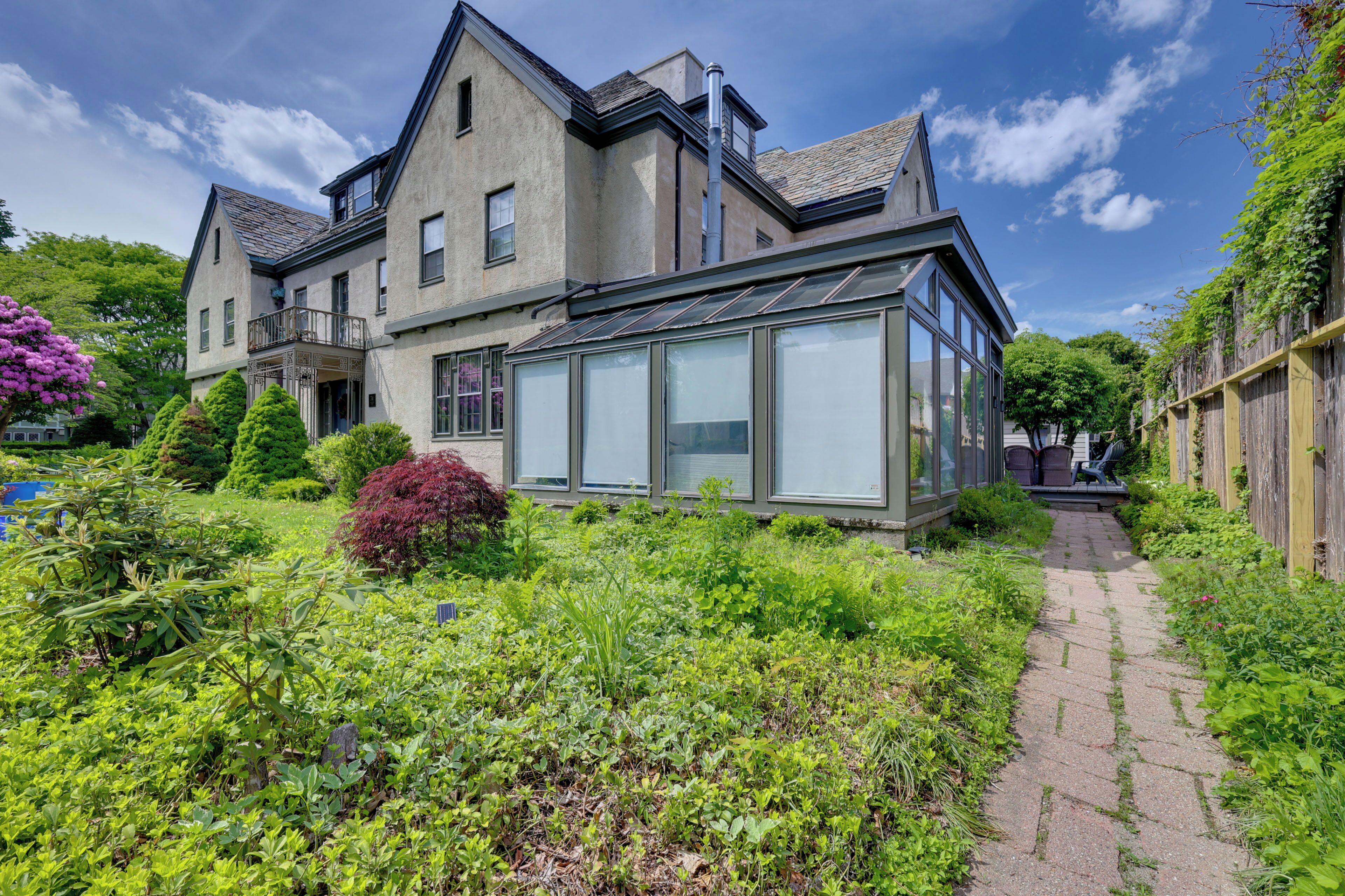 A large house with a conservatory, a garden with various plants, and a paved pathway.