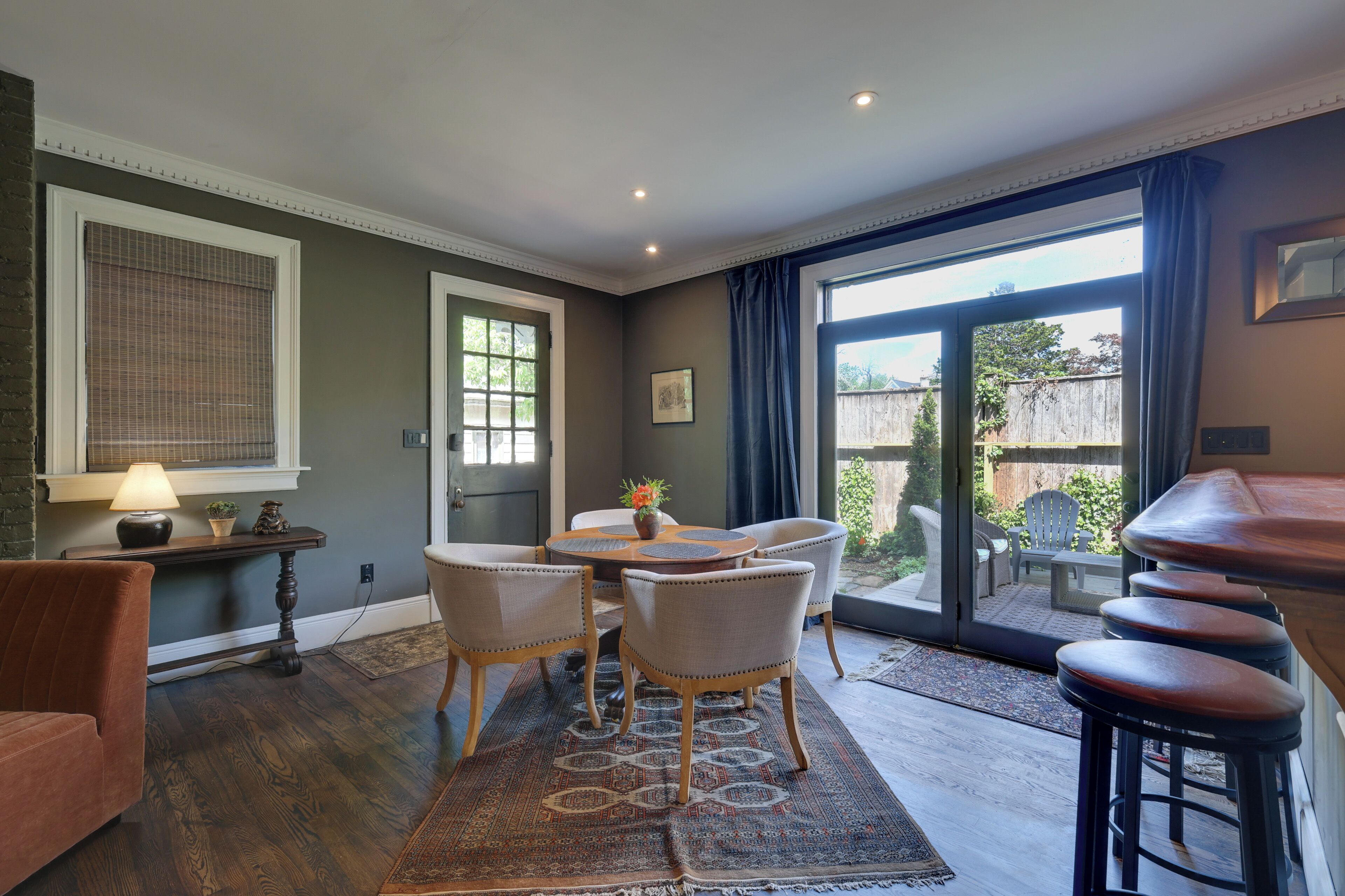 A dining area with a table and chairs, a bar stool area, and a view through a glass door.
