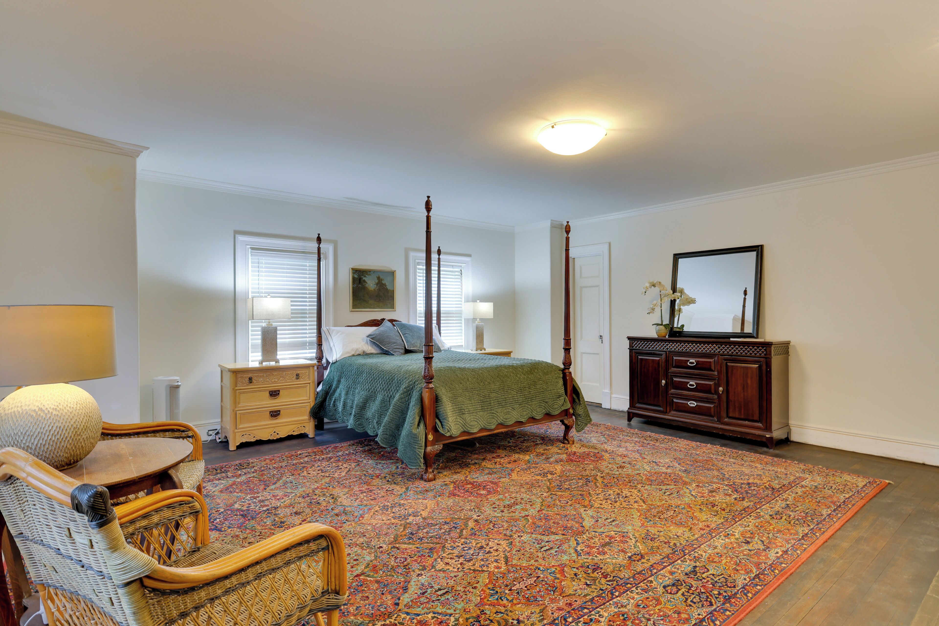 A bedroom with a four-poster bed, a dresser, a chair, and a large rug.