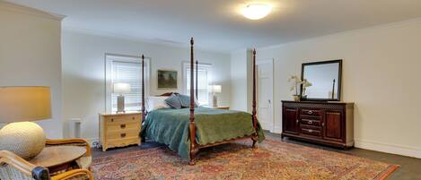 A bedroom with a four-poster bed, a dresser, a chair, and a large rug.