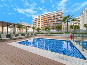 A rooftop pool with lounge chairs, a pergola, and a modern building in the background. - Bloomfields 2BR in Azizi Riviera Azure (Dubai)