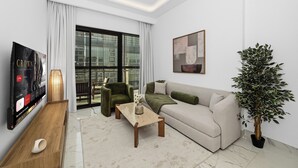 A modern living room with a sofa, a coffee table, a TV, and a large window. - Bloomfields 2BR in Azizi Riviera 51  (Dubai)