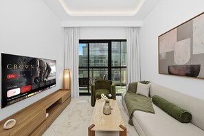 Ein modernes Wohnzimmer mit einem großen Flachbildfernseher, einem grünen Sessel, einer Couch und einem Couchtisch.
