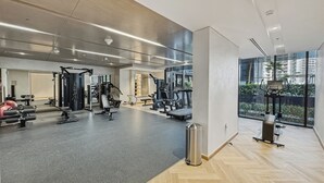 A modern gym with various exercise equipment, large windows, and a herringbone floor pattern. - Bloomfields 2BR in Azizi Riviera 51  (Dubai)