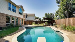 Un patio trasero con piscina, una terraza de madera y zona delimitada por una cerca.