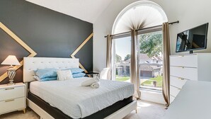 Un dormitorio con cama, mesitas de noche, lámpara, televisor y vistas al exterior.