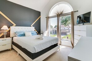 Ein Schlafzimmer mit einem Bett, Nachttischen, einer Lampe, einem Fernseher und Blick ins Freie.