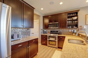 A modern kitchen with stainless steel appliances, wooden cabinets, a tiled backsplash, and a granite countertop. - Hot Tub, Mtn Views, Resort Perks! Granby Getaway (Granby)