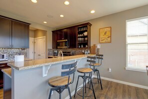 Une cuisine avec des meubles en bois foncé, un four à micro-ondes en acier inoxydable, un dosseret carrelé et un coin bar avec des tabourets.