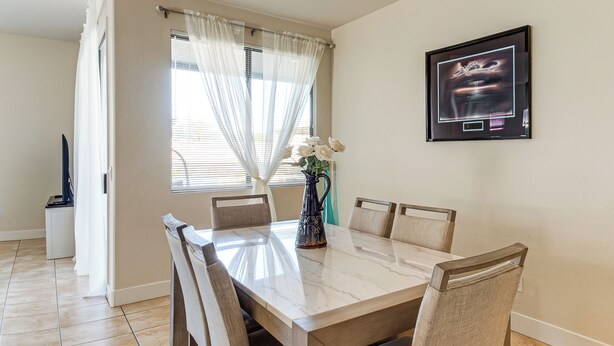 A dining area with a marble table, six chairs, a vase with flowers, a framed picture on the wall, and a window with sheer curtains. - 5 Mi to Estrella Mtn Park! Home w/ Outdoor Oasis (Goodyear)