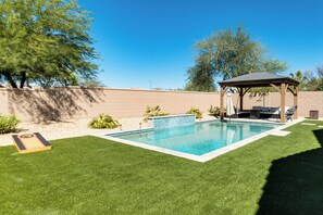 A rectangular swimming pool with a wooden gazebo, surrounded by a well-maintained lawn and a brick wall. - 5 Mi to Estrella Mtn Park! Home w/ Outdoor Oasis (Goodyear)