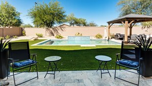 A backyard with a swimming pool, artificial grass, and outdoor furniture. - 5 Mi to Estrella Mtn Park! Home w/ Outdoor Oasis (Goodyear)