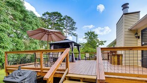 Un patio in legno con barbecue coperto, posti a sedere all'aperto e un gazebo.