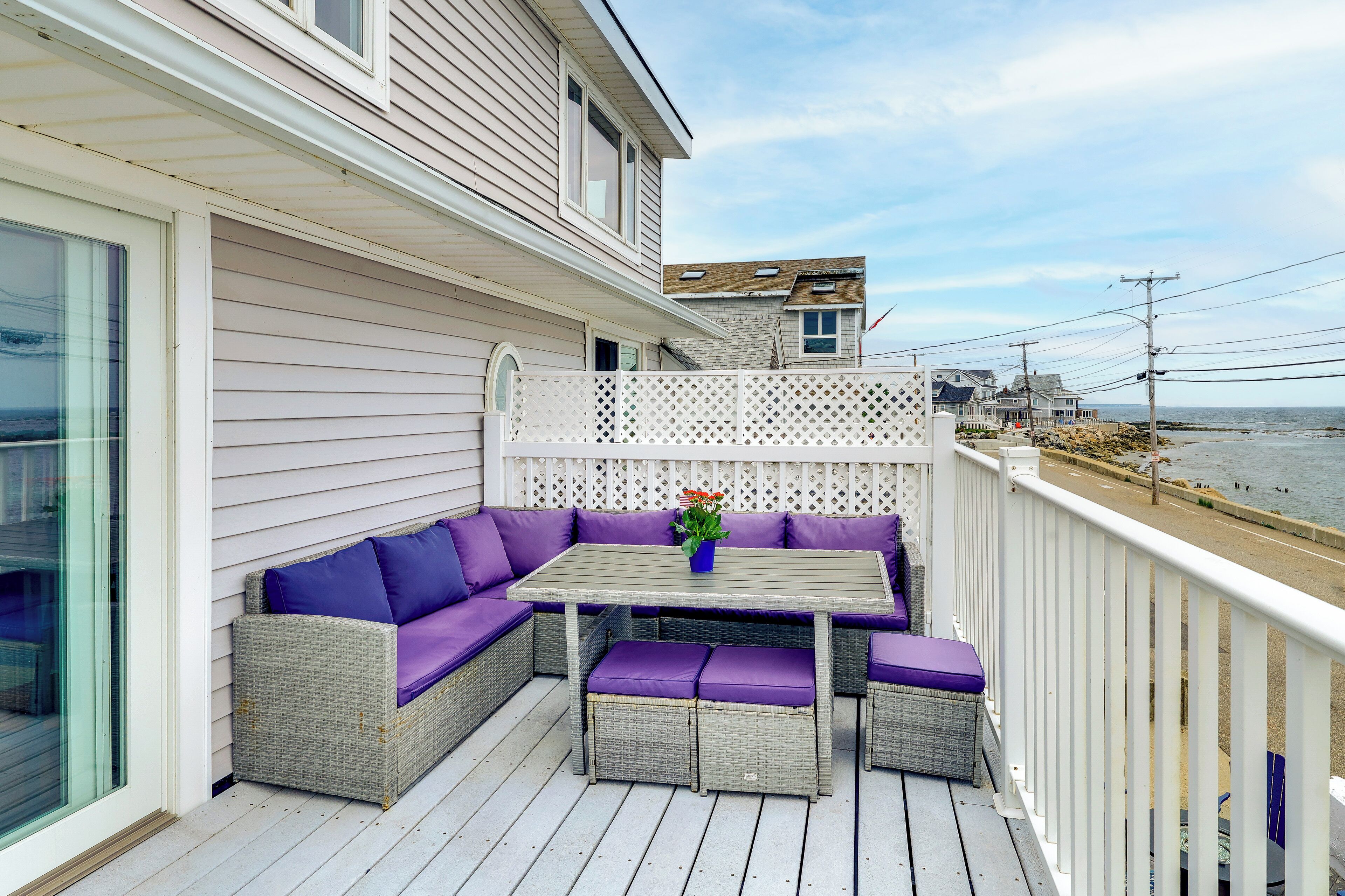 A balcony with a wicker sofa and table, overlooking a beach.