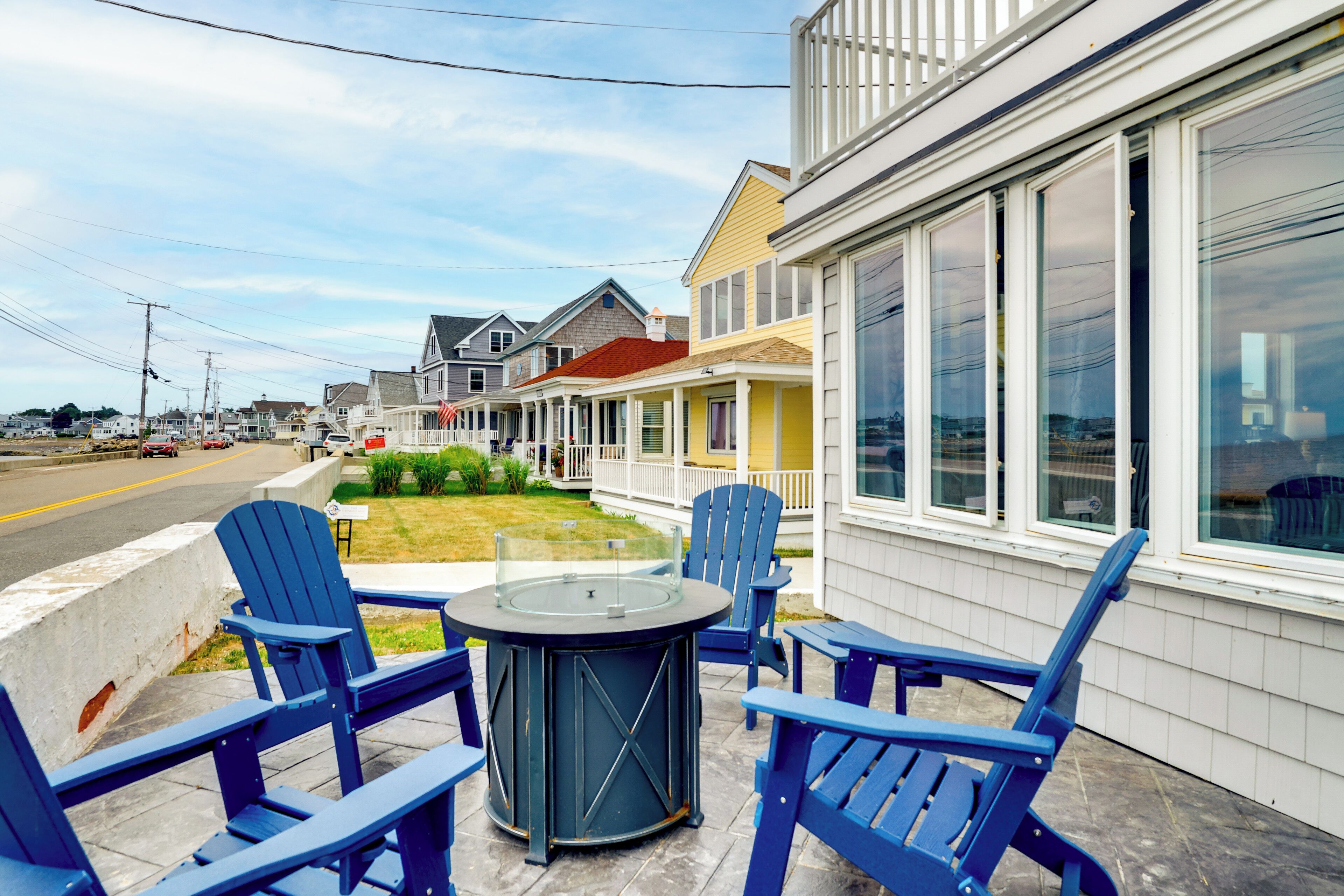 A waterfront property with a patio area featuring blue Adirondack chairs and a round table.