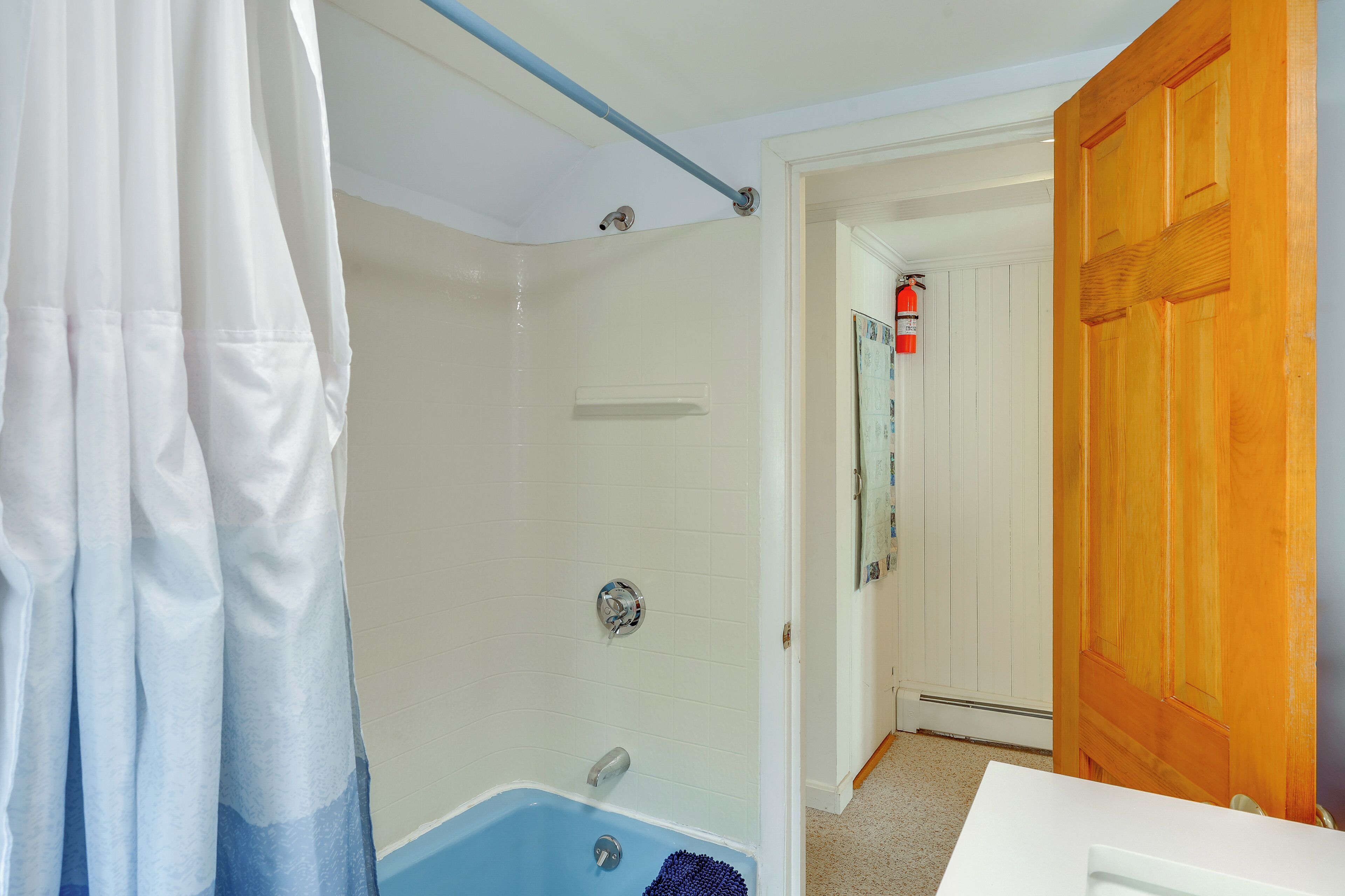 Een badkamer met een bad, douchegordijn en een houten deur.