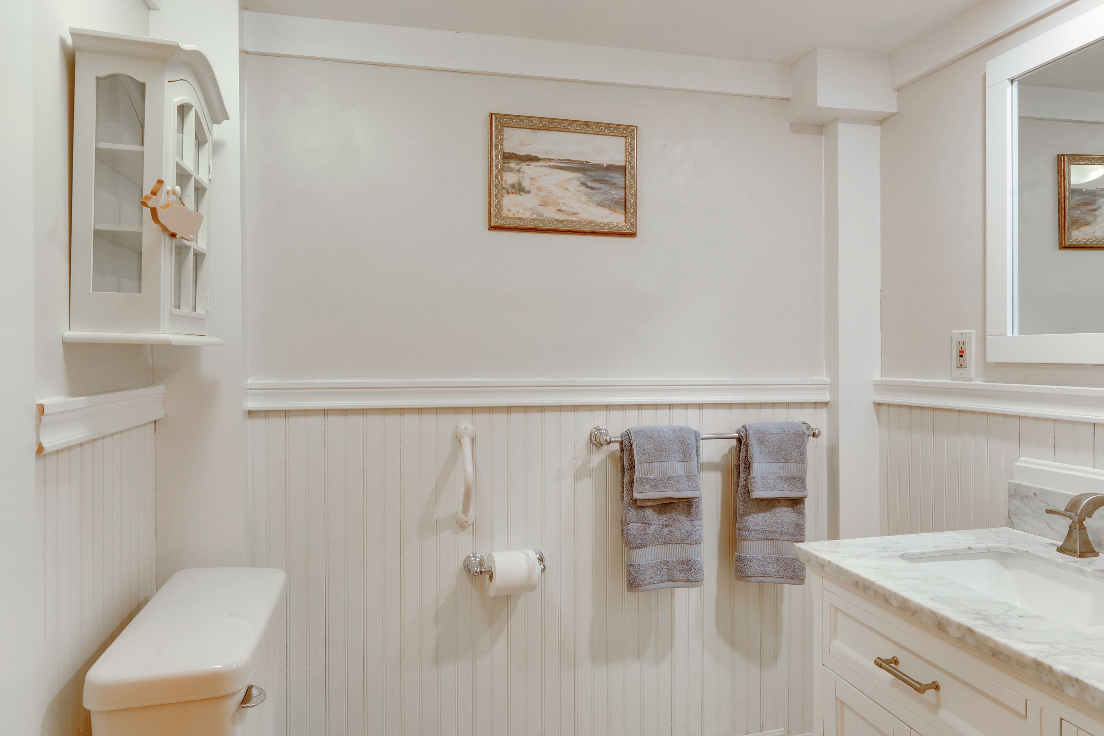 A bathroom with a toilet, sink, and mirror. There are towels hanging on a towel bar.
