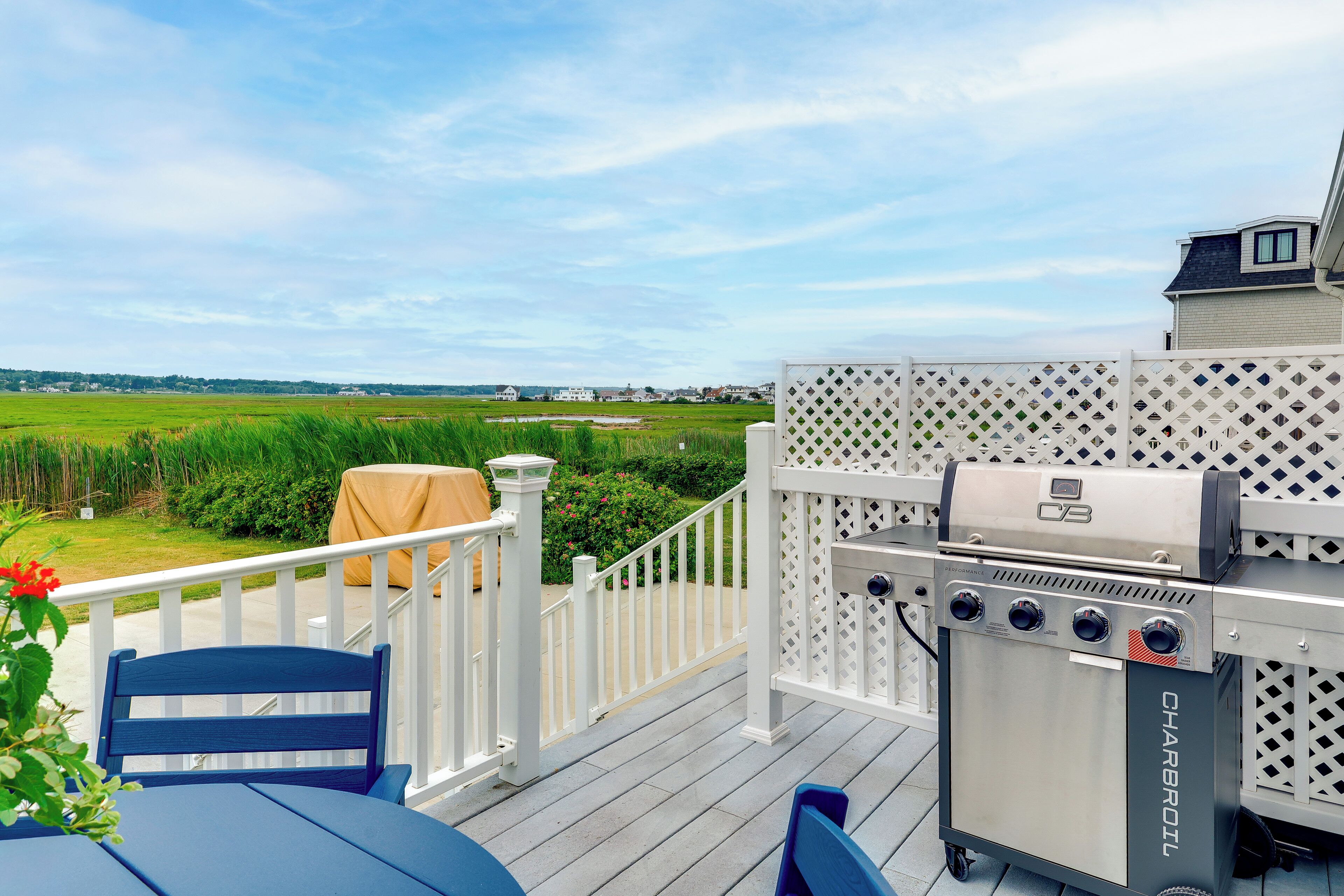 A deck with a grill, chairs, and a view of a green field.