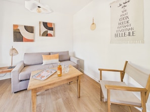 A modern living room with a sofa, a wooden coffee table, a chair, and abstract wall art. - Apartment for 4 - Shared Garden - Terrace - WiFi (Fouesnant)
