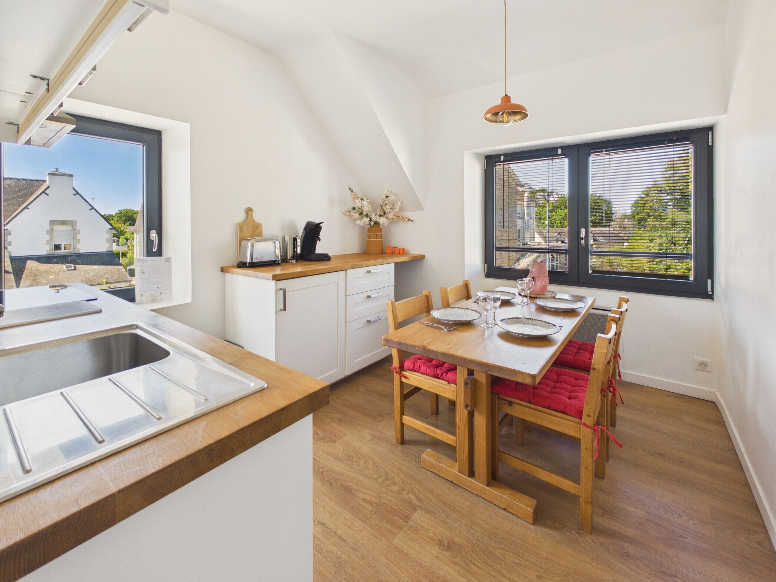 A modern kitchen with a wooden countertop, a dining table set for four, and a view of the outside through a window.