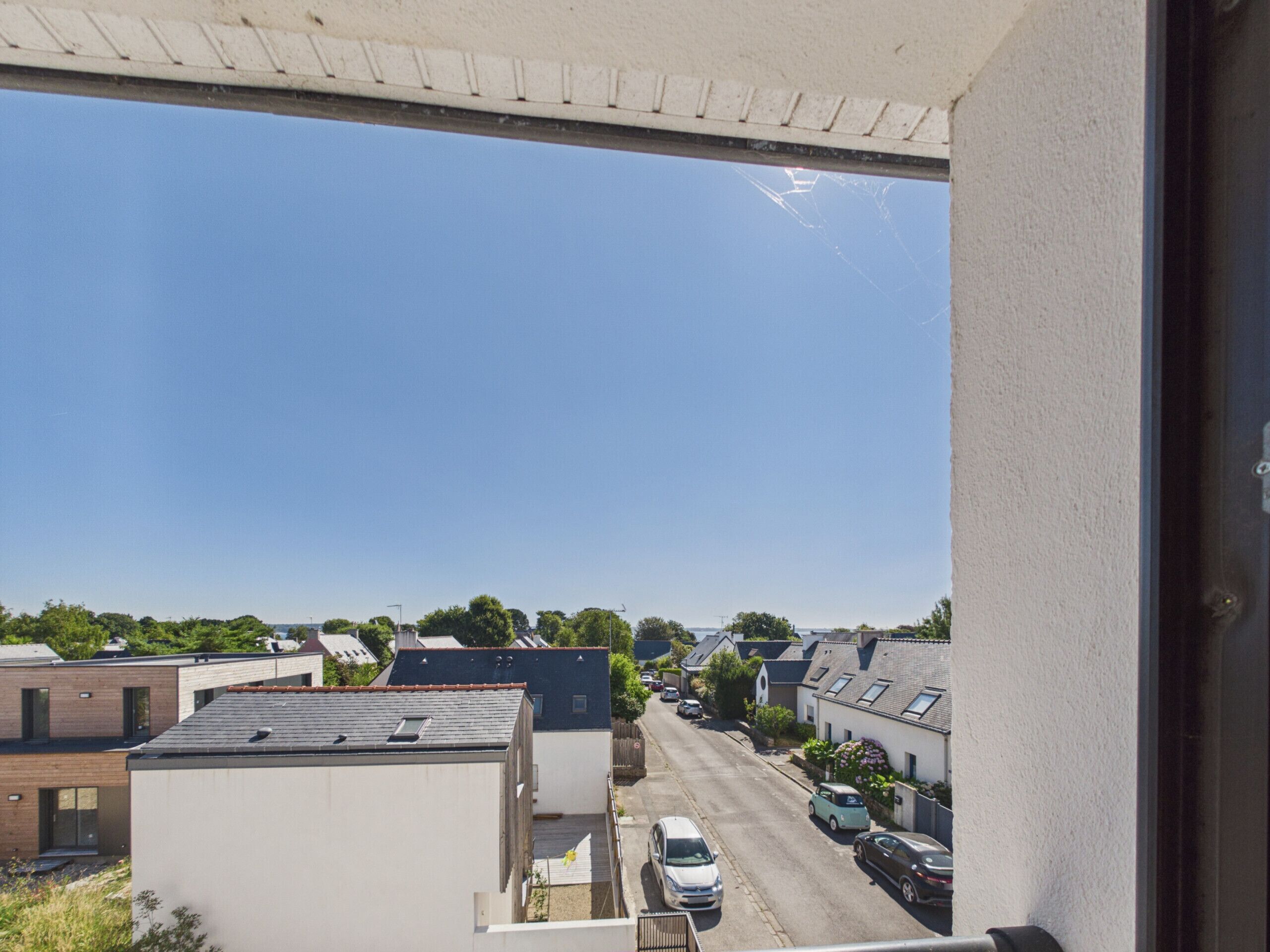 Una calle residencial con casas, coches estacionados a un lado y un cielo azul despejado.
