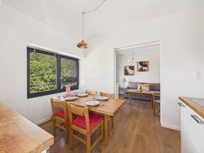 Ein Essbereich mit Holztisch, gedeckt für vier Personen, einem Fenster mit Jalousien und einer Couch im Hintergrund.