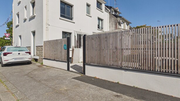 A white building with a gated entrance, a parked car, and a clear blue sky. - Apartment for 4 - Shared Garden - Terrace - WiFi (Fouesnant)
