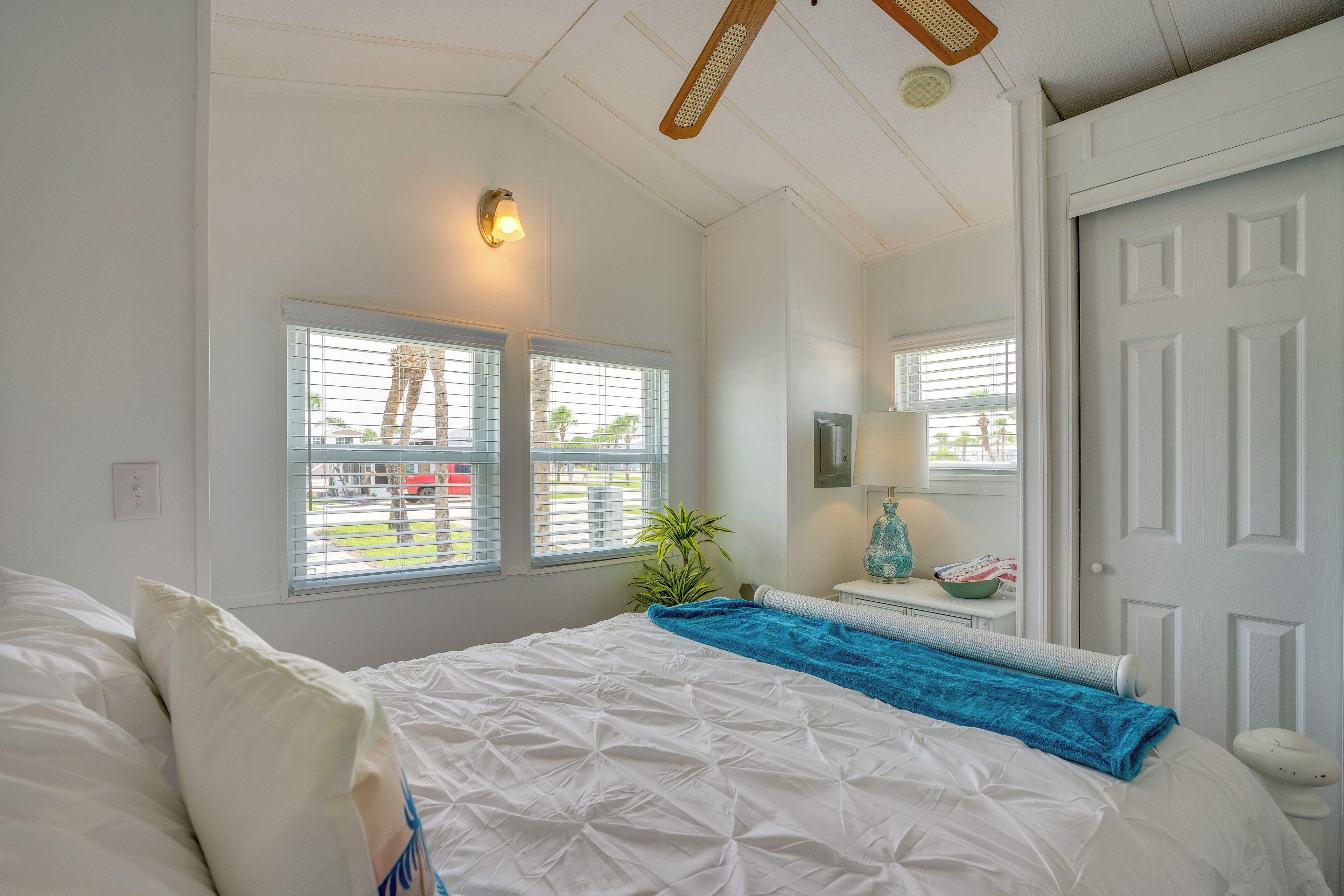 A bedroom with a bed, two windows, a ceiling fan, a nightstand, and a door.