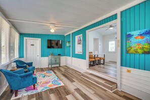A room with teal walls, a wooden floor, a dining area with a table and chairs, and a TV mounted on the wall. - 5 Mi to Fort Myers Beach! Home w/ Resort Perks (Fort Myers)